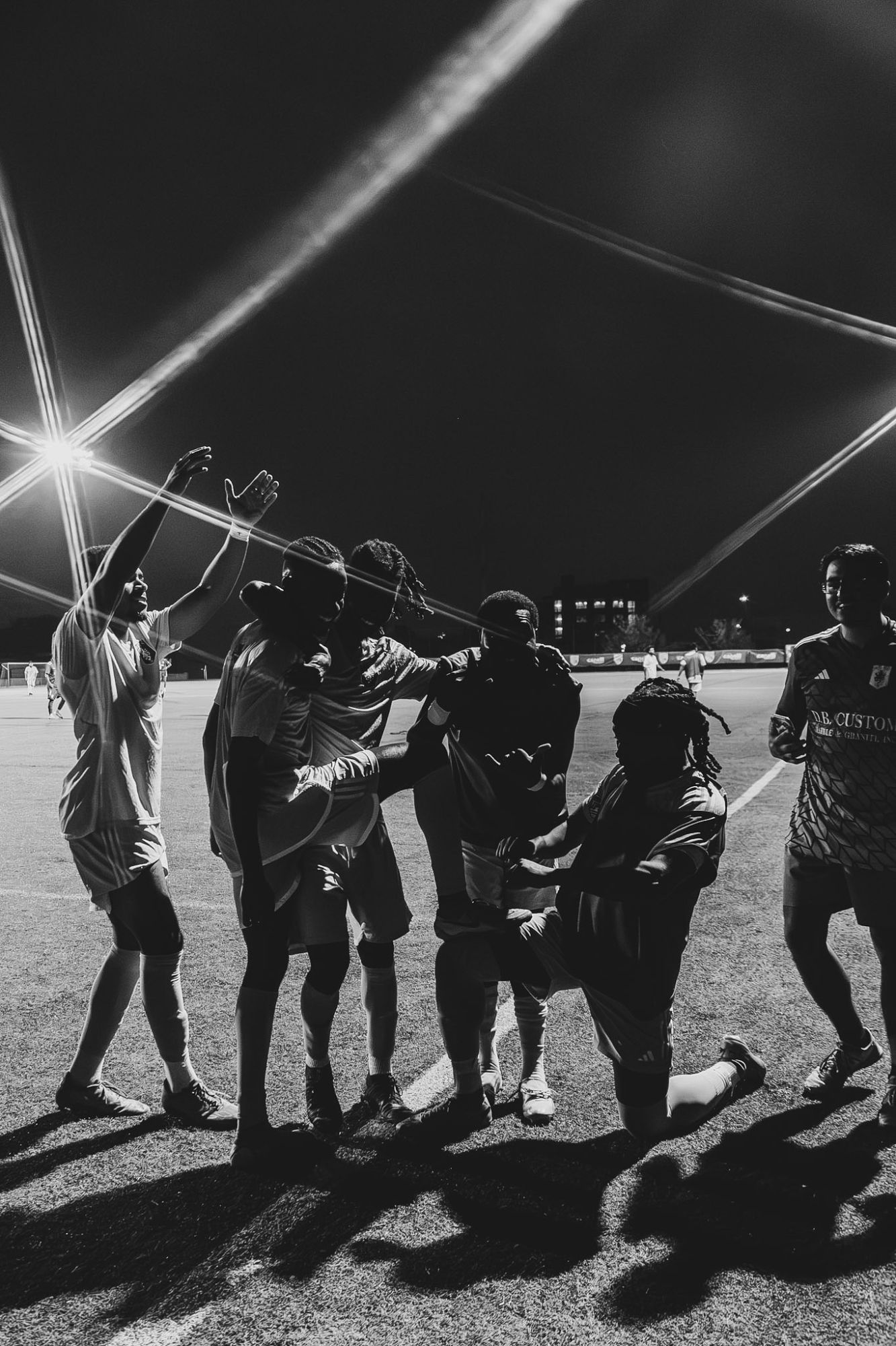Alexandria United FC players celebrating together under the floodlights